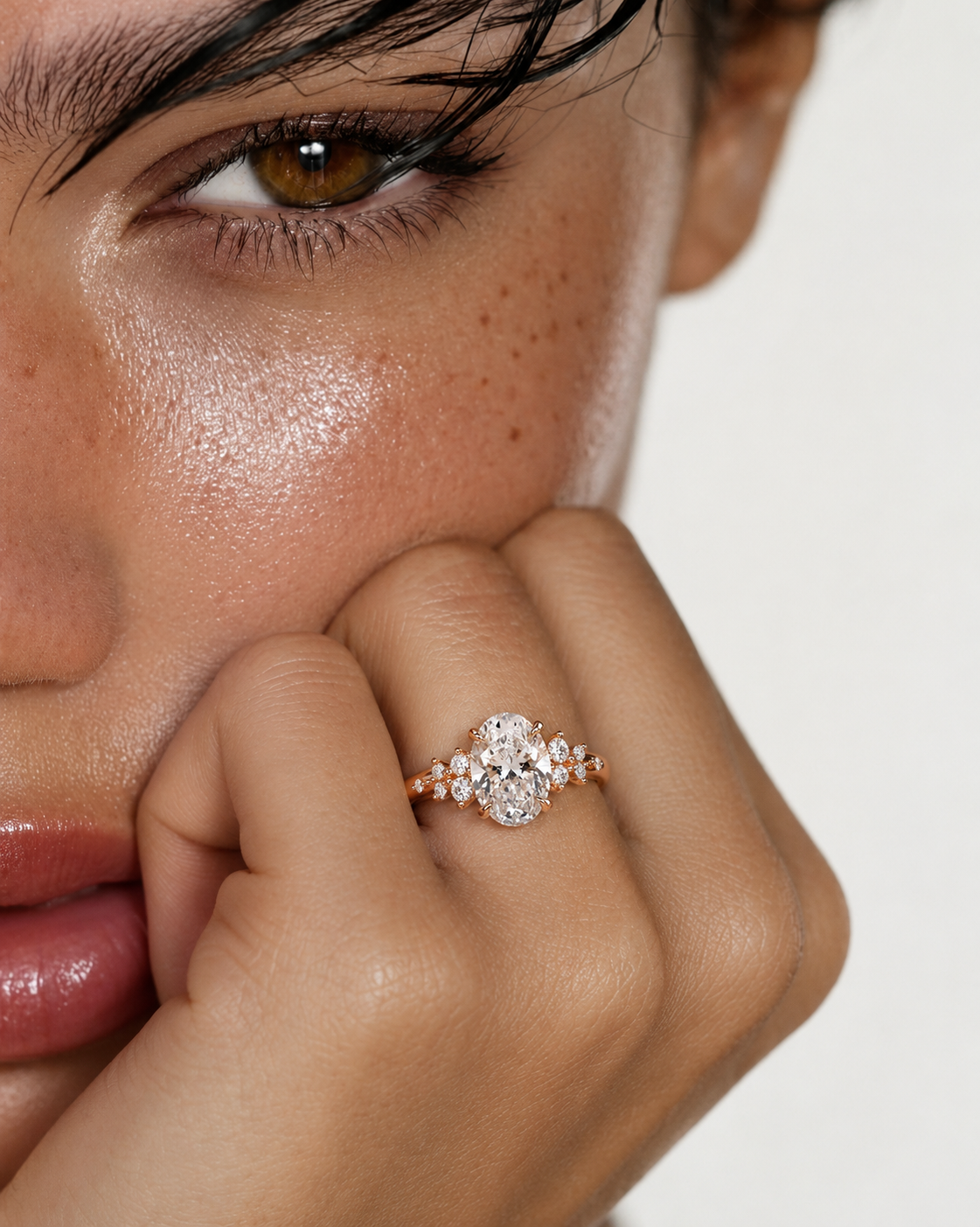 color_10K_RG, color_14K_RG &&A close-up lifestyle shot of a model wearing a rose gold ring with a clear floral cluster center stone and smaller side stones, resting on her finger near her face.