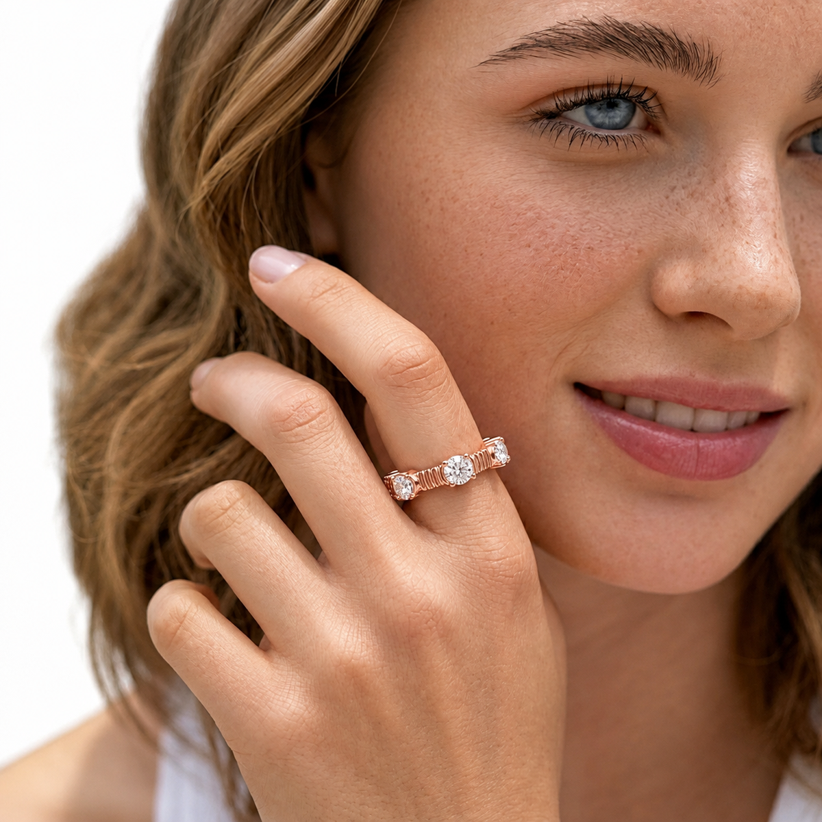 color_10K_RG, color_14K_RG &&	A close-up lifestyle shot of a woman wearing a rose gold band ring with three round-cut clear gemstones. The ring is shown on her finger against a clean white background.