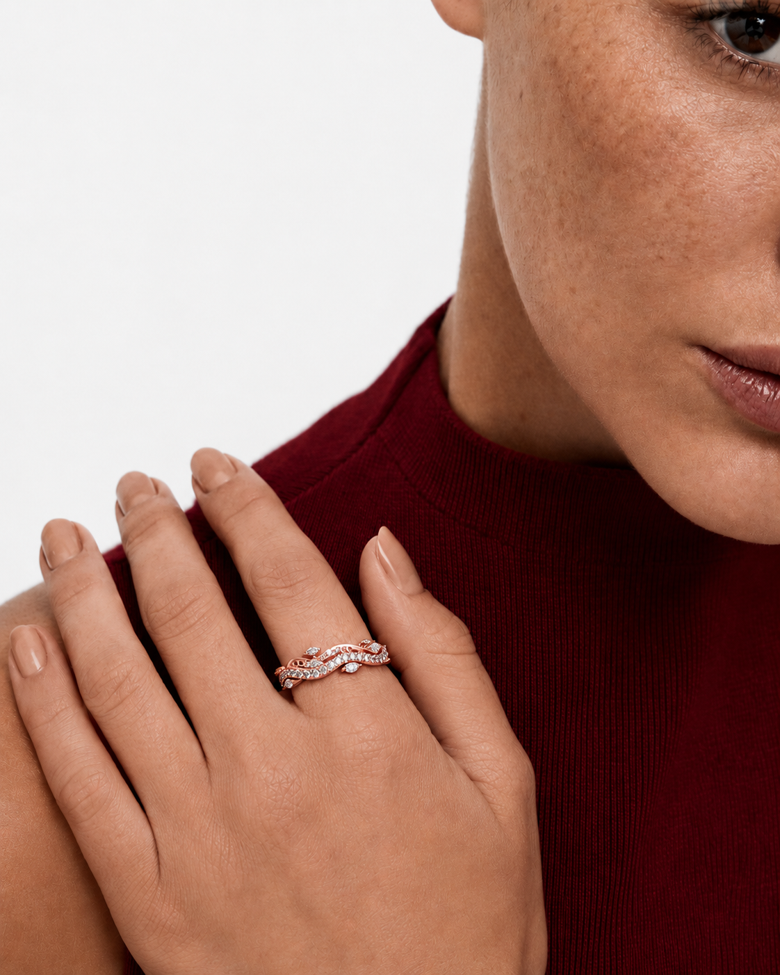 color_10K_RG, color_14K_RG &&	A close-up lifestyle shot of a woman wearing a delicate, wavy rose gold ring set with small clear stones on her ring finger. She is wearing a dark red ribbed knit top against a clean white background.