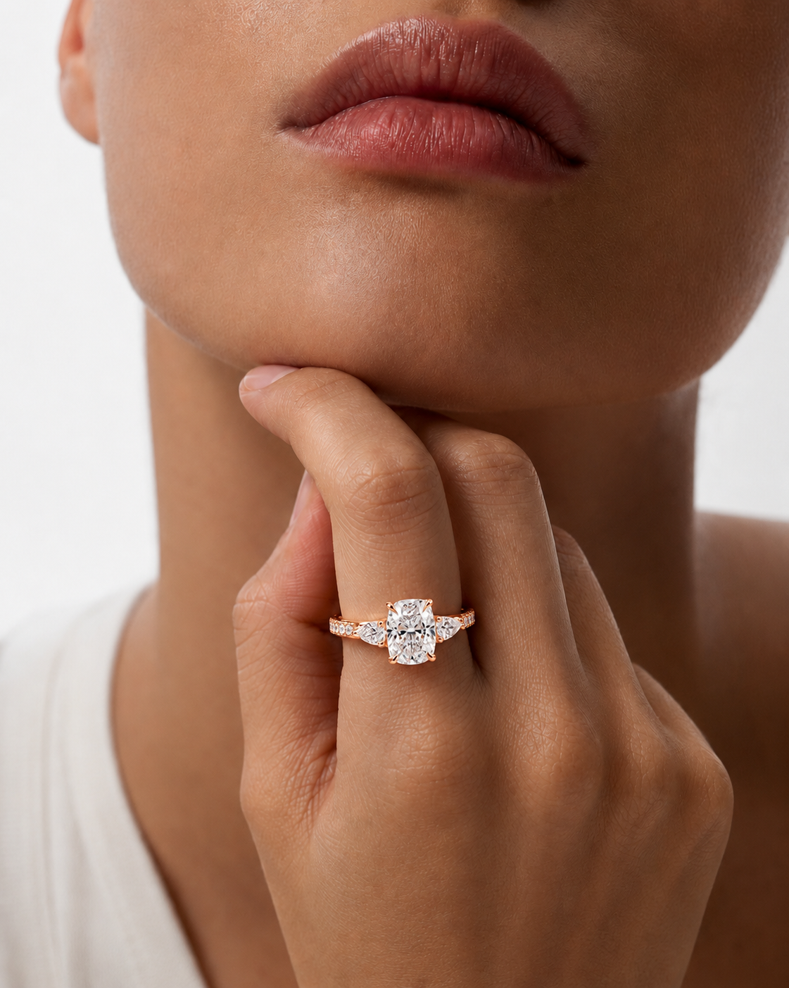 color_10K_RG, color_14K_RG &&A close-up lifestyle shot of a model wearing a rose gold ring with a clear marquise-cut center stone and smaller round stones, resting on her finger.