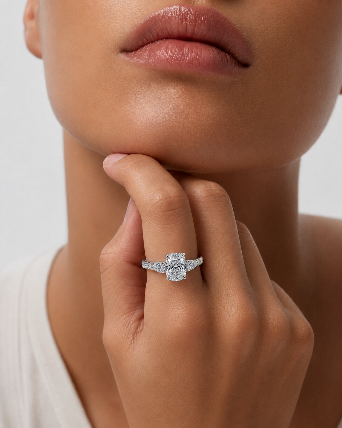 color_925_SIL,color_935_ARG,color_10K_WG, color_14K_WG &&A close-up lifestyle shot of a model wearing a silver-toned diamond engagement ring on her finger, with her hand resting on her chin against a clean light gray background.