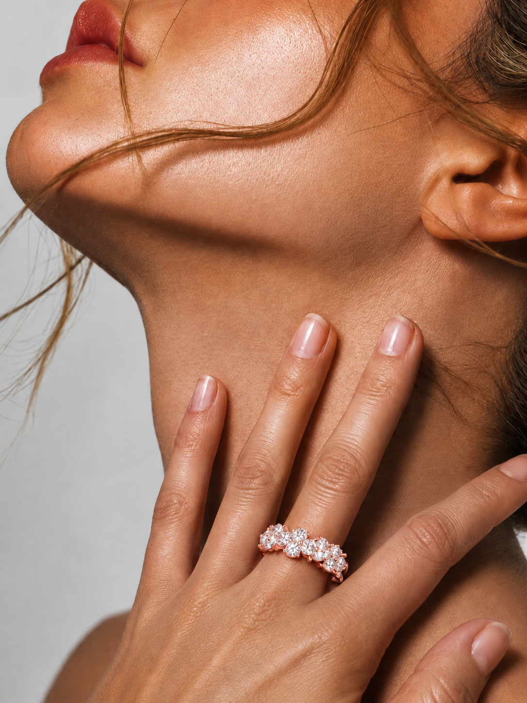 color_10K_RG, color_14K_RG &&	A close-up lifestyle shot of a model's hand resting on her neck, wearing a delicate rose gold band ring set with small clear cubic zirconia stones.
