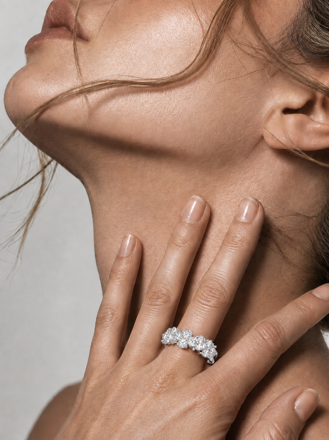 color_925_SIL,color_935_ARG,color_10K_WG, color_14K_WG &&	
A close-up lifestyle shot of a model's neck and hand, wearing a silver-toned diamond ring with a cluster of sparkling stones.