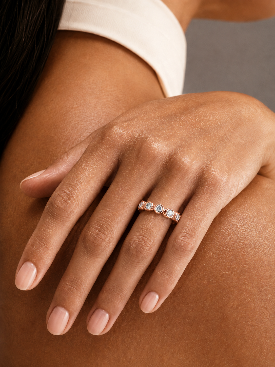 color_10K_RG, color_14K_RG &&	A close-up of a woman's hand resting on her shoulder, wearing a delicate rose gold band ring with small round-cut clear gemstones.