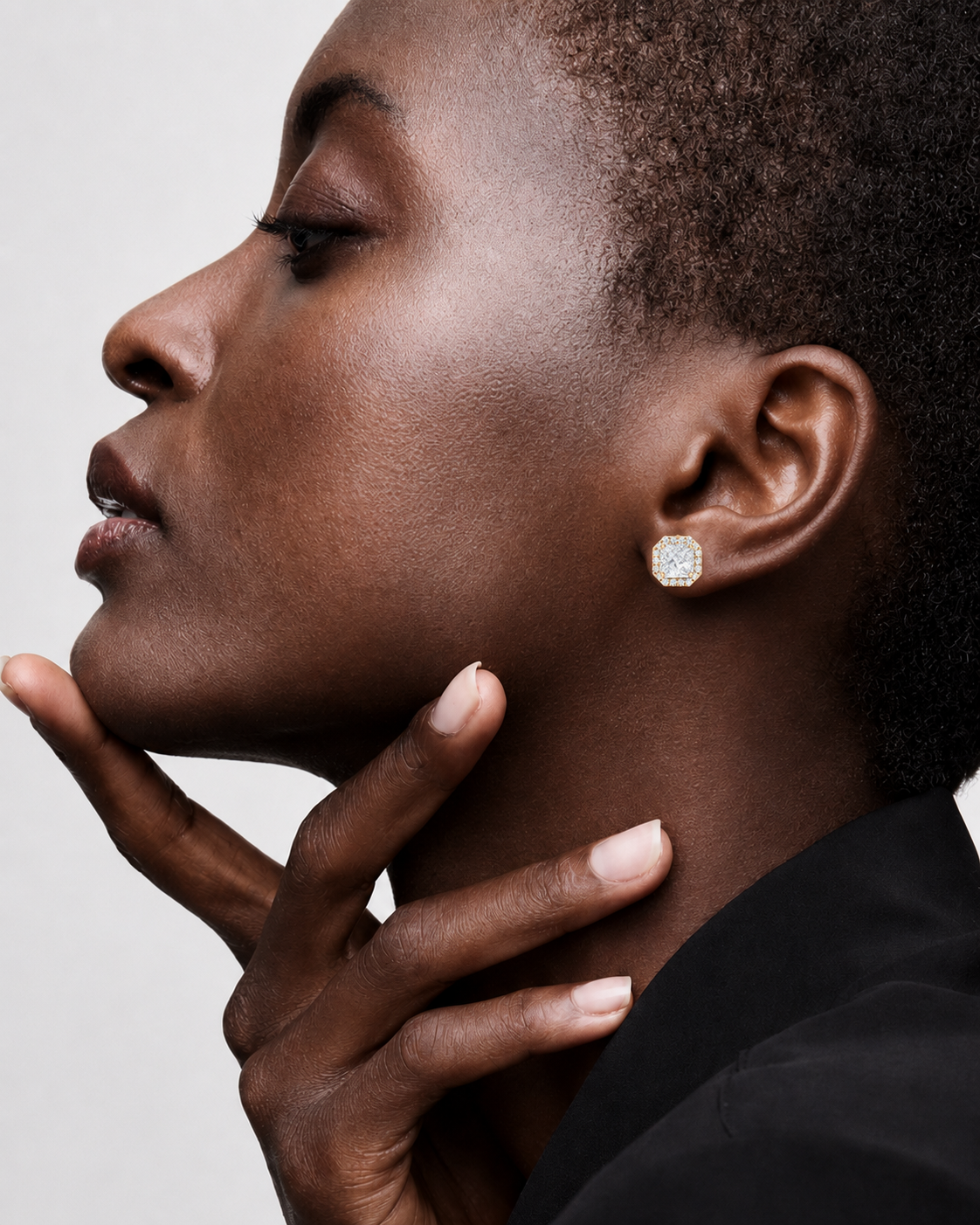 color_10K_YG, color_14K_YG &&A close-up side profile of a model wearing a small, round, bezel-set clear gemstone earring on one ear, with her hand resting near her chin against a light gray background.