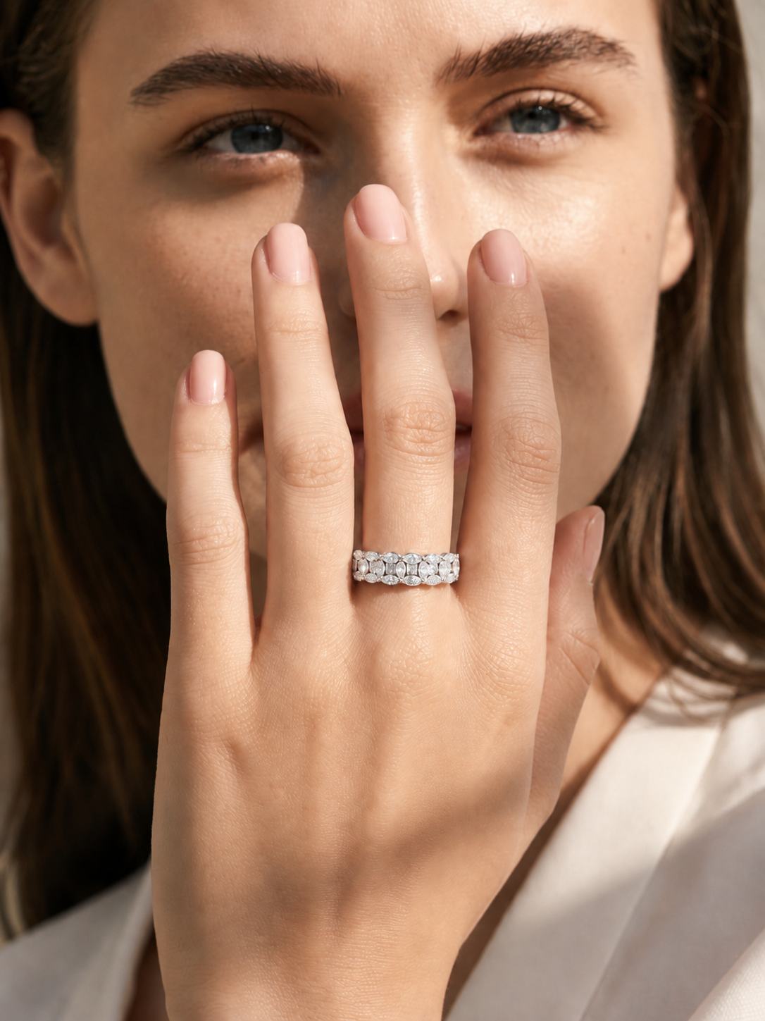 color_925_SIL,color_935_ARG,color_10K_WG, color_14K_WG &&	
A close-up lifestyle shot of a woman wearing a sparkling diamond eternity ring on her finger, with her hand covering part of her face.