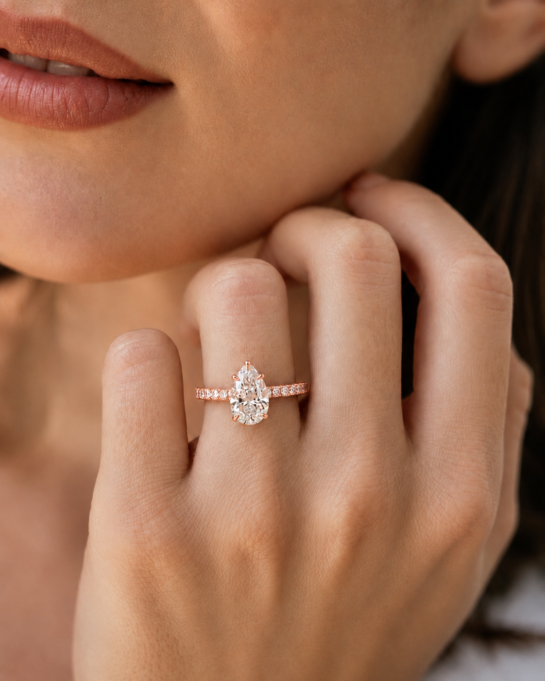 color_10K_RG, color_14K_RG &&A close-up lifestyle shot of a woman wearing a rose gold ring with a pear-cut diamond and small side stones on her finger.