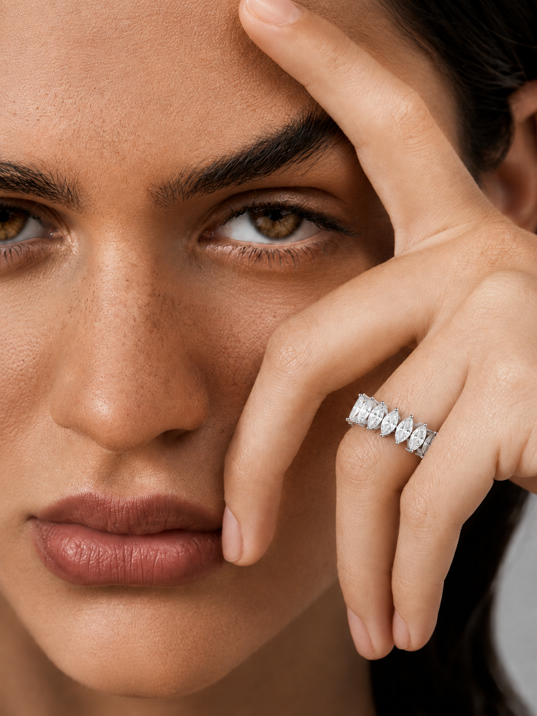 color_925_SIL,color_935_ARG,color_10K_WG, color_14K_WG &&	
A close-up of a model's face and hand wearing a silver marquise-cut stone ring on her finger.