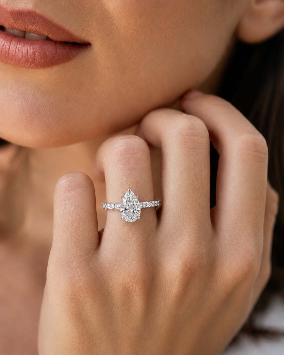 color_925_SIL,color_935_ARG,color_10K_WG, color_14K_WG &&A close-up lifestyle shot of a woman wearing a silver ring with a pear-cut diamond and small side stones on her finger.