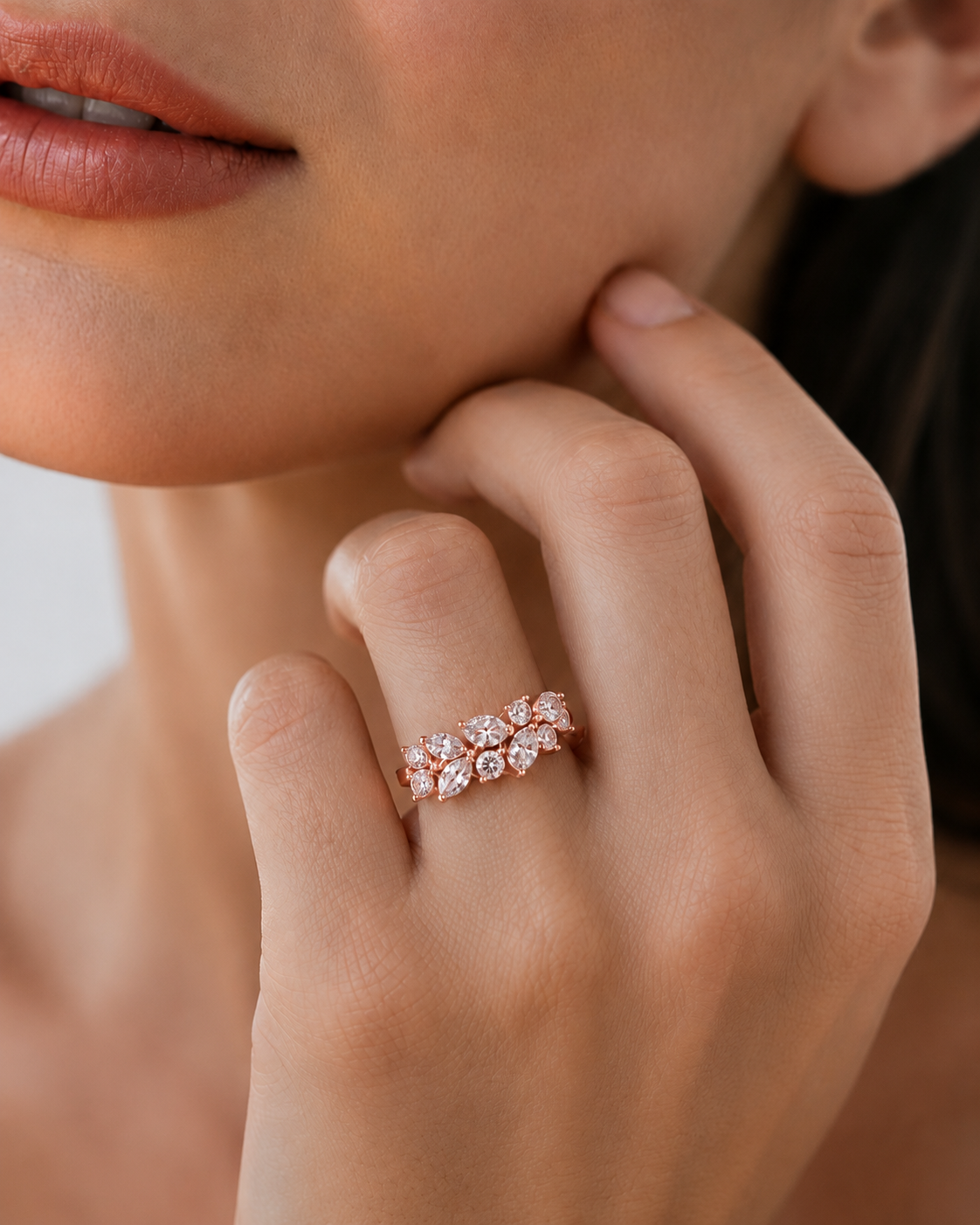 color_10K_RG, color_14K_RG &&	A close-up lifestyle shot of a model's hand wearing a delicate rose gold band ring set with small clear gemstones.