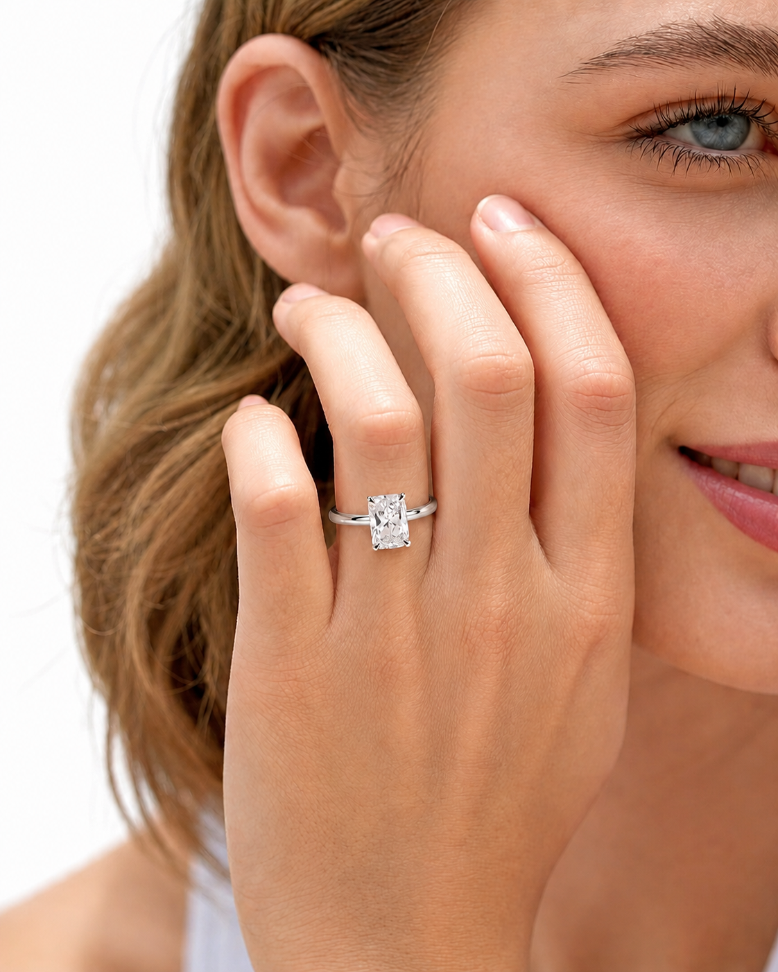 color_925_SIL,color_935_ARG,color_10K_WG, color_14K_WG &&A close-up lifestyle shot of a woman wearing a silver engagement ring with a rectangular clear gemstone on her finger, with her hand resting against her cheek against a white background.