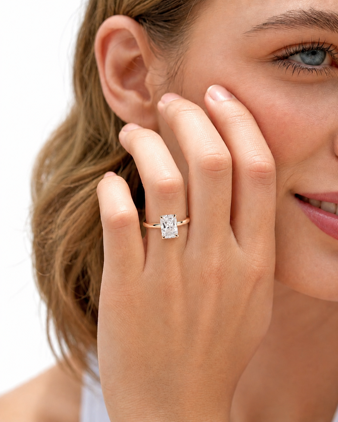 color_10K_RG, color_14K_RG &&A close-up lifestyle shot of a woman wearing a gold ring with a rectangular clear gemstone on her finger, with her hand resting against her cheek against a white background.