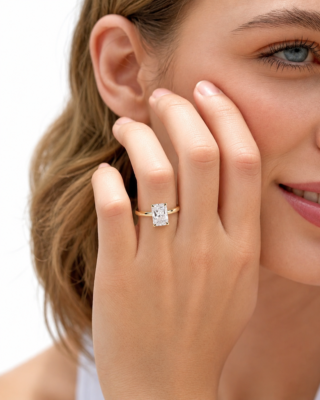 color_10K_YG, color_14K_YG &&A close-up lifestyle shot of a woman wearing a gold ring with a rectangular clear gemstone on her finger, with her hand resting against her cheek against a white background.
