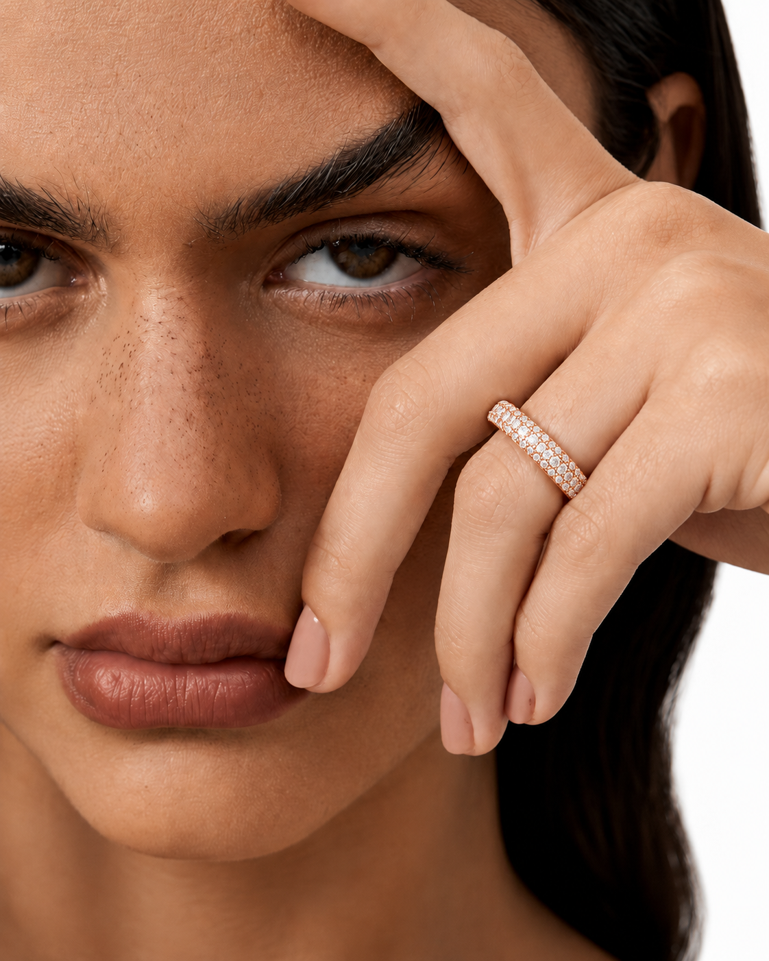 color_10K_RG, color_14K_RG &&	A close-up lifestyle shot of a model wearing a delicate rose gold band ring set with small clear pave stones on her ring finger, against a clean white background.