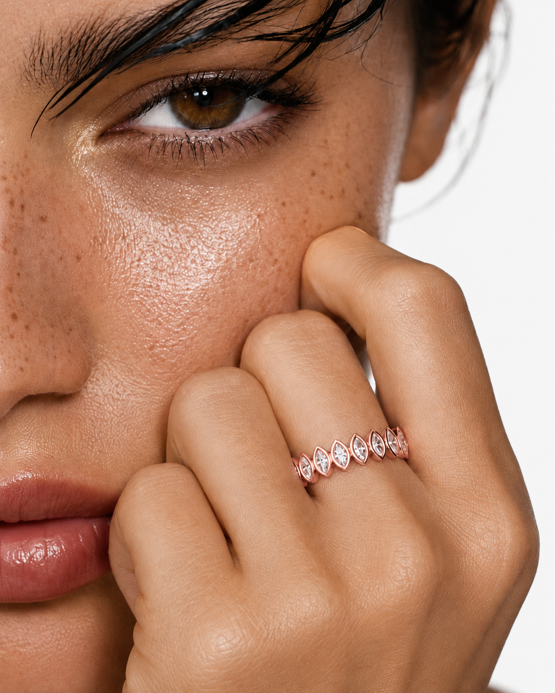 color_10K_RG, color_14K_RG &&	A close-up lifestyle shot of a model wearing a delicate rose gold band ring with marquise-cut clear stones on her finger, with her hand resting near her face against a clean white background.