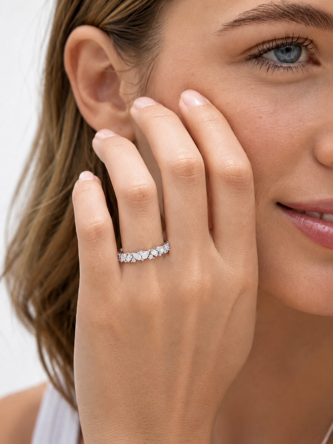 color_925_SIL,color_935_ARG,color_10K_WG, color_14K_WG &&	
A close-up lifestyle shot of a woman wearing a silver diamond eternity ring on her finger, with her hand resting against her cheek.