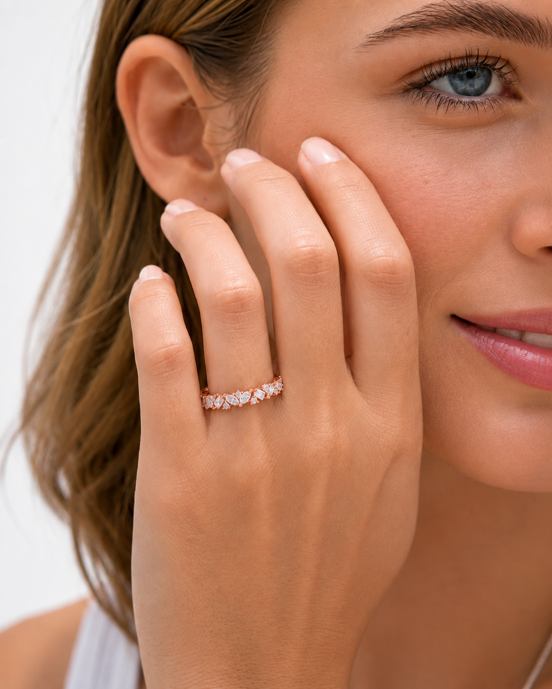 color_10K_RG, color_14K_RG &&	A close-up lifestyle shot of a woman wearing a delicate rose gold band ring with small clear stones on her finger, set against a clean white background.
