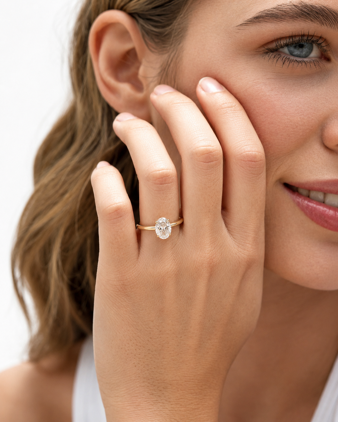 color_10K_YG, color_14K_YG &&A close-up lifestyle shot of a woman wearing a gold ring with a round-cut clear gemstone on her finger, with her hand resting against her cheek against a clean white background.