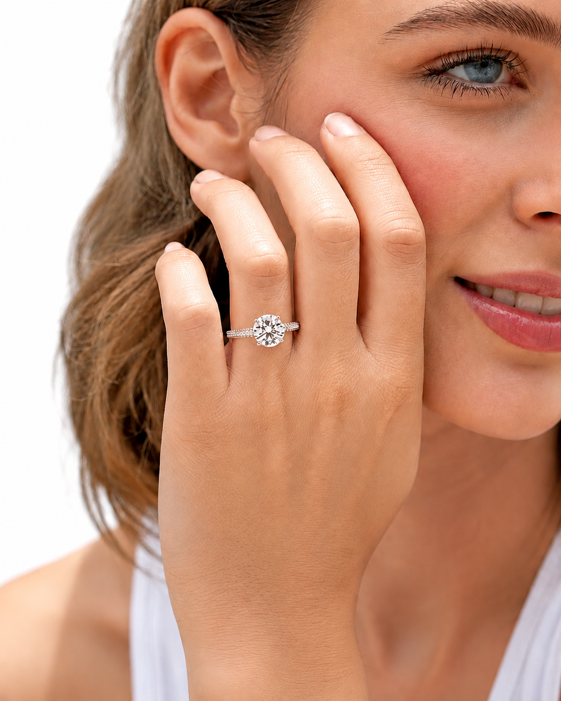 color_925_SIL,color_935_ARG,color_10K_WG, color_14K_WG &&A close-up lifestyle shot of a woman wearing a silver-toned diamond engagement ring on her finger, with her hand resting against her cheek against a clean white background.