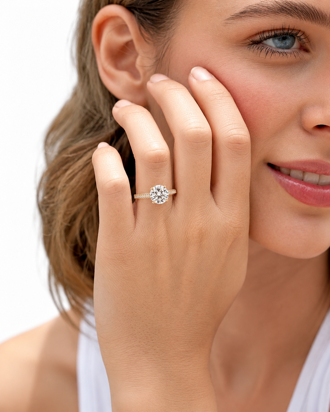 color_10K_YG, color_14K_YG &&A close-up lifestyle shot of a woman wearing a round-cut diamond engagement ring on a gold band, with her hand resting against her cheek against a clean white background.