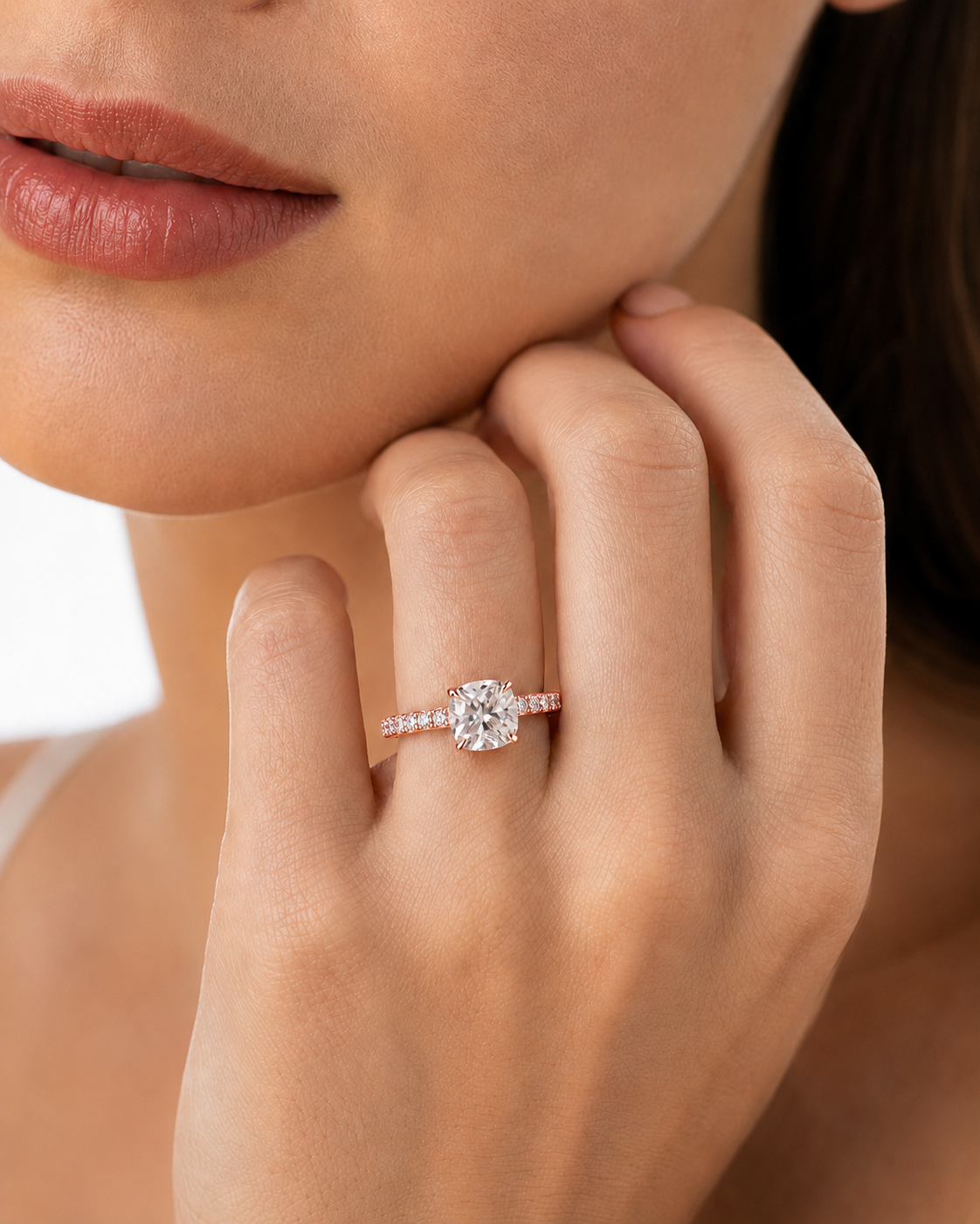 color_10K_RG, color_14K_RG &&A close-up lifestyle shot of a woman wearing a diamond engagement ring on her finger, with her hand resting near her chin.