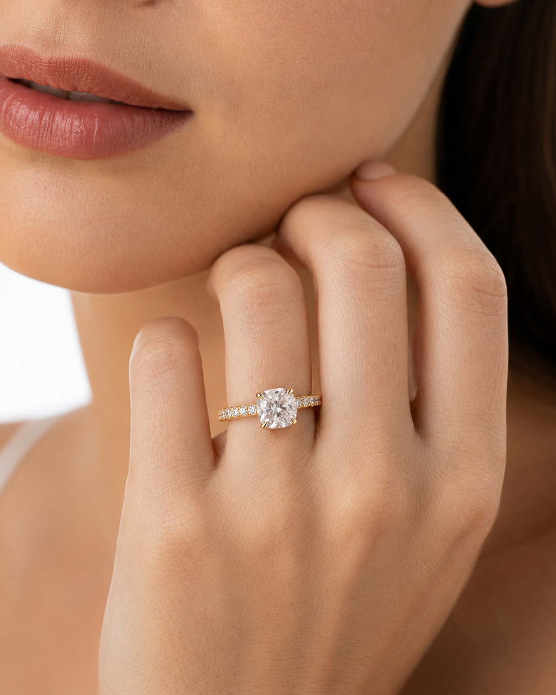 color_10K_YG, color_14K_YG &&A close-up lifestyle shot of a woman wearing a diamond engagement ring on her finger. The ring features a round-cut center stone with a delicate yellow gold band accented by small pave diamonds.