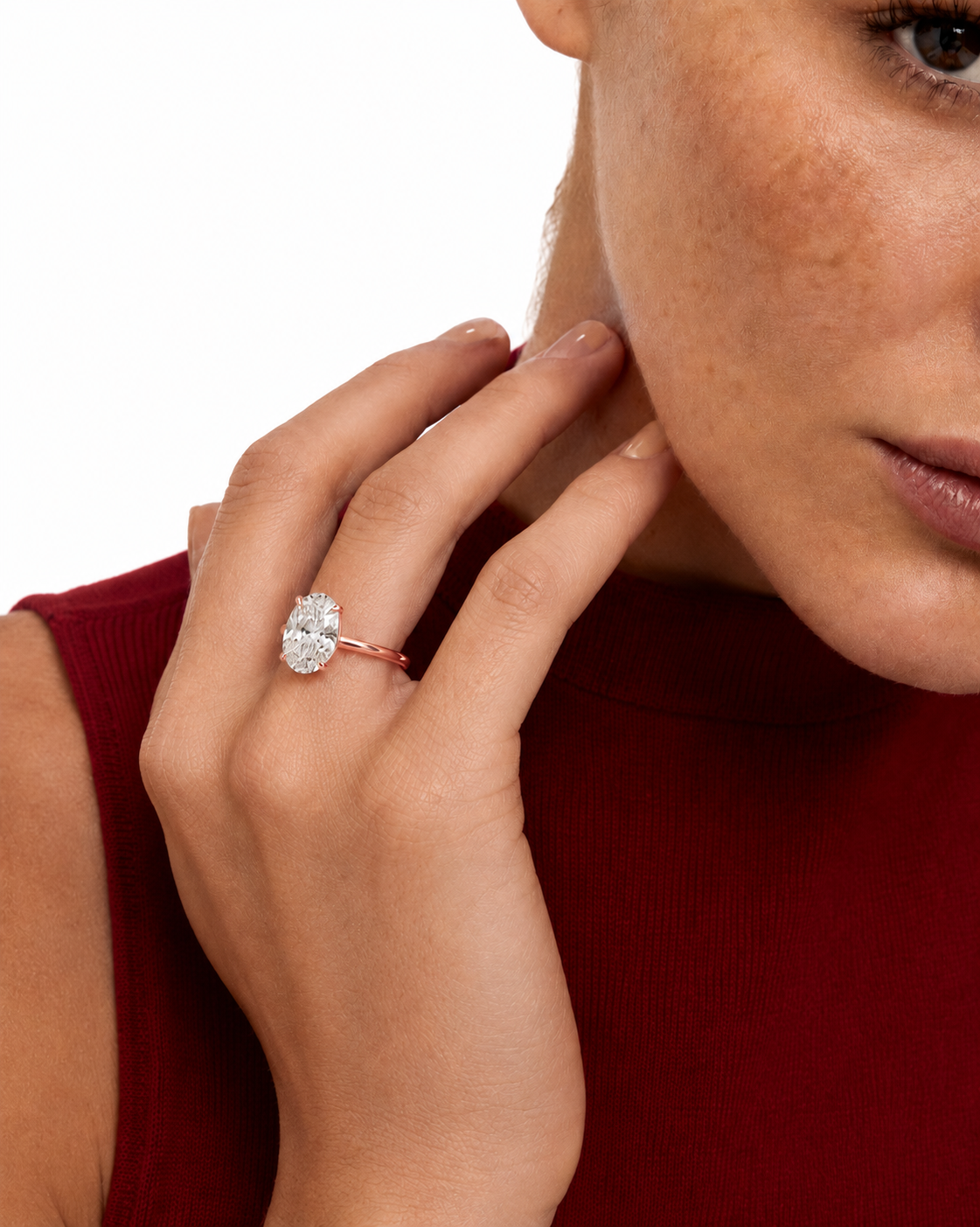 color_10K_RG, color_14K_RG &&A close-up lifestyle shot of a model wearing a rose gold ring with a large oval-cut clear gemstone. The model is wearing a dark red ribbed top, and the background is a clean white studio backdrop.