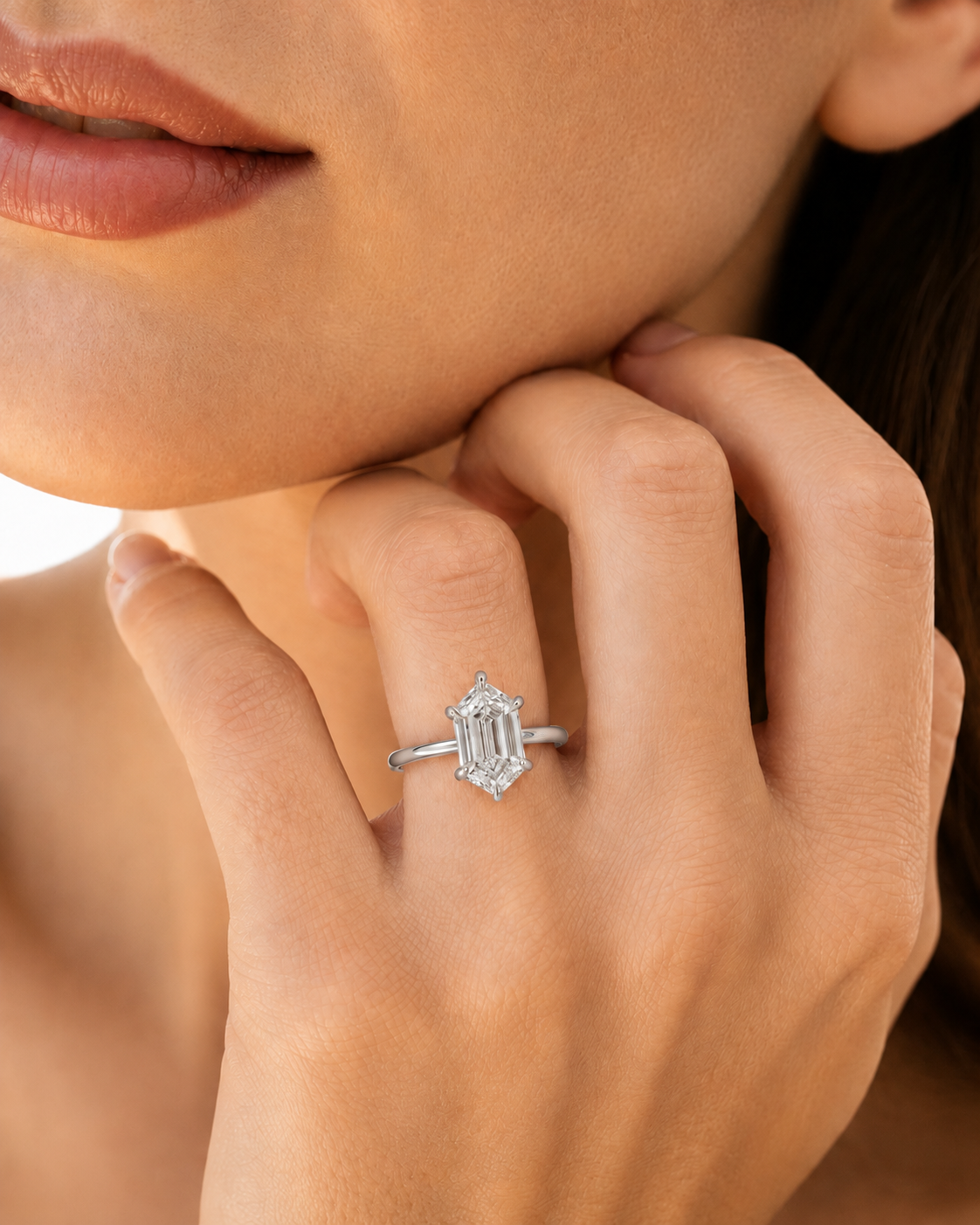 color_925_SIL,color_935_ARG,color_10K_WG, color_14K_WG &&A close-up of a woman's hand wearing a silver-toned ring with an emerald-cut diamond. The ring is shown on her ring finger against a soft, warm-toned background.