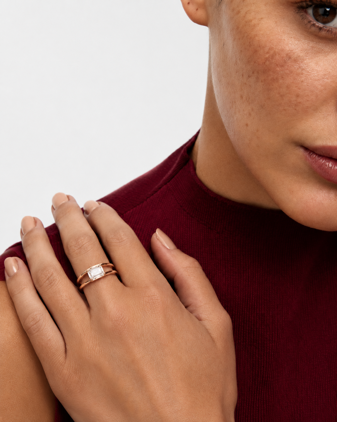 color_10K_RG, color_14K_RG &&A close-up lifestyle shot of a model wearing a rose gold ring with a rectangular clear gemstone on her finger, paired with a dark red ribbed top against a light gray background.