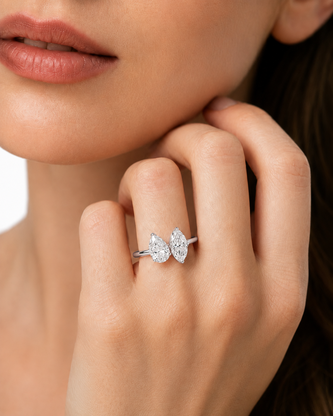color_925_SIL,color_935_ARG,color_10K_WG, color_14K_WG &&A close-up lifestyle shot of a model wearing a silver ring with two pear-cut clear gemstones on her finger.