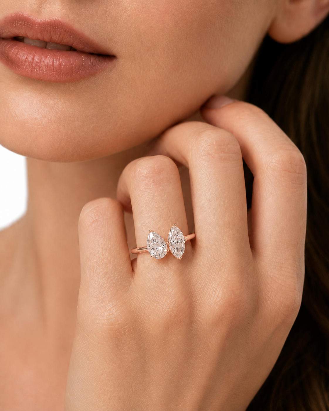 color_10K_RG, color_14K_RG &&A close-up lifestyle shot of a model wearing a delicate rose gold ring with two pear-cut diamond clusters on the ring finger.