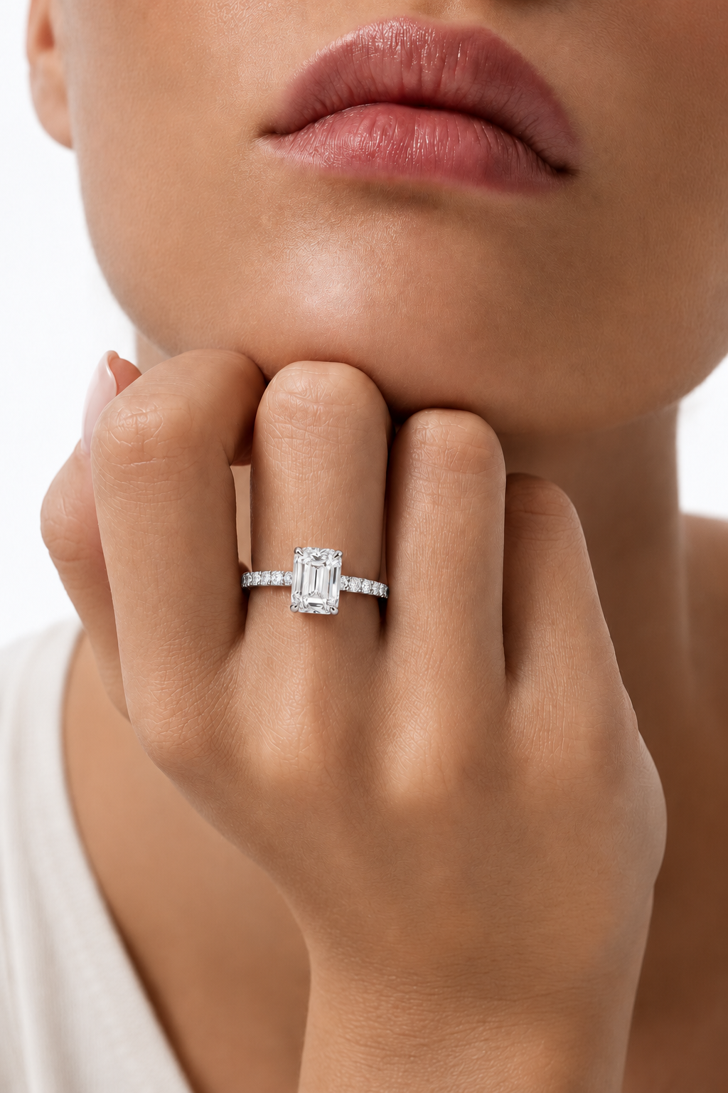 color_925_SIL,color_935_ARG,color_10K_WG, color_14K_WG &&A close-up lifestyle shot of a model wearing a silver engagement ring with an emerald-cut center stone and small side stones.