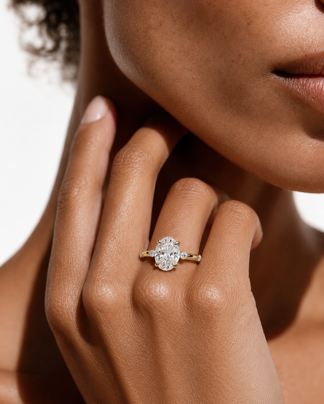 color_10K_YG, color_14K_YG &&A close-up lifestyle shot of a model's hand wearing a diamond engagement ring with a gold band. The ring features a central round-cut diamond surrounded by a halo of smaller diamonds, set on a gold band with small side stones.