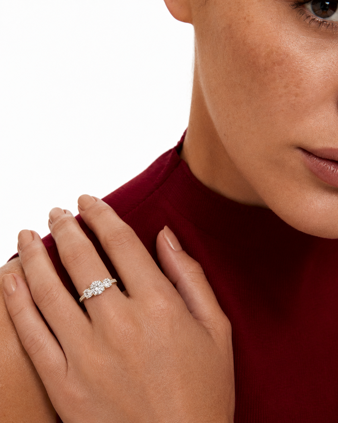 color_10K_YG, color_14K_YG &&A close-up lifestyle shot of a woman wearing a delicate diamond ring on her finger, resting her hand on her shoulder. She is wearing a deep burgundy mock-neck top against a clean white background.