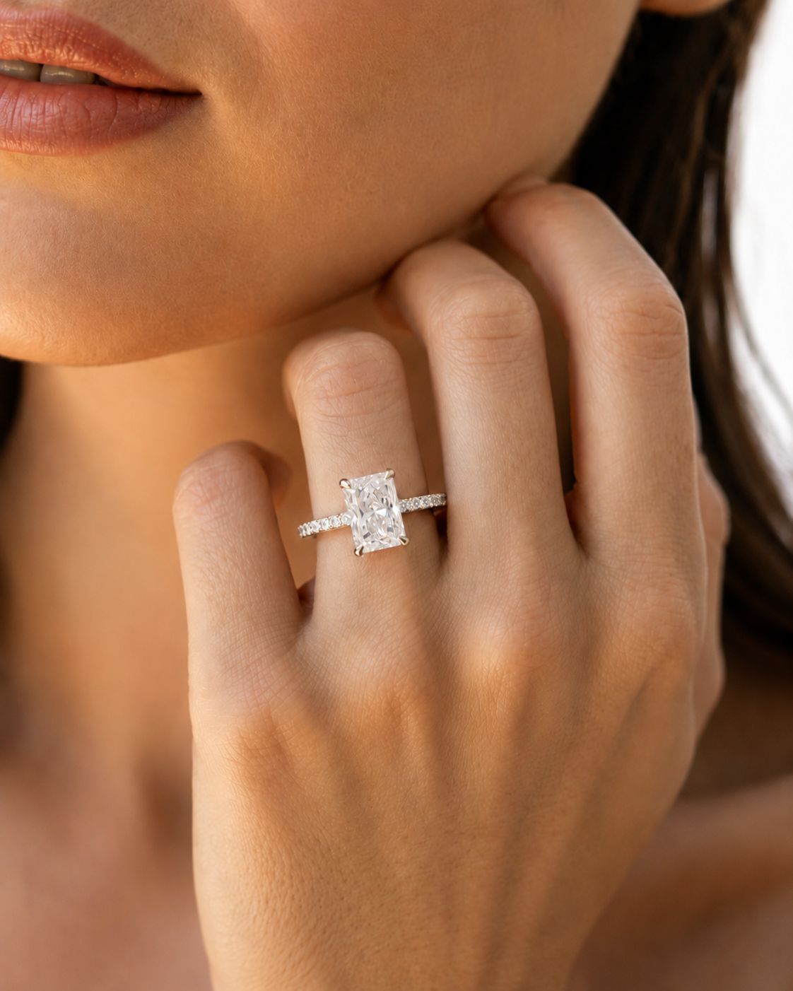 color_925_SIL,color_935_ARG,color_10K_WG, color_14K_WG &&A close-up lifestyle shot of a model wearing a silver engagement ring with a rectangular clear center stone and a pave band on her finger.