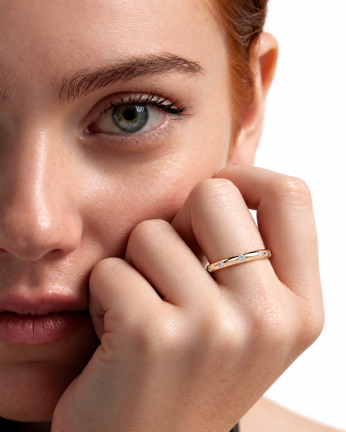 color_10K_YG, color_14K_YG &&A 
A close-up lifestyle shot of a model wearing a thin gold band ring with a small clear gemstone on her finger, with her hand resting against her cheek against a white background.
