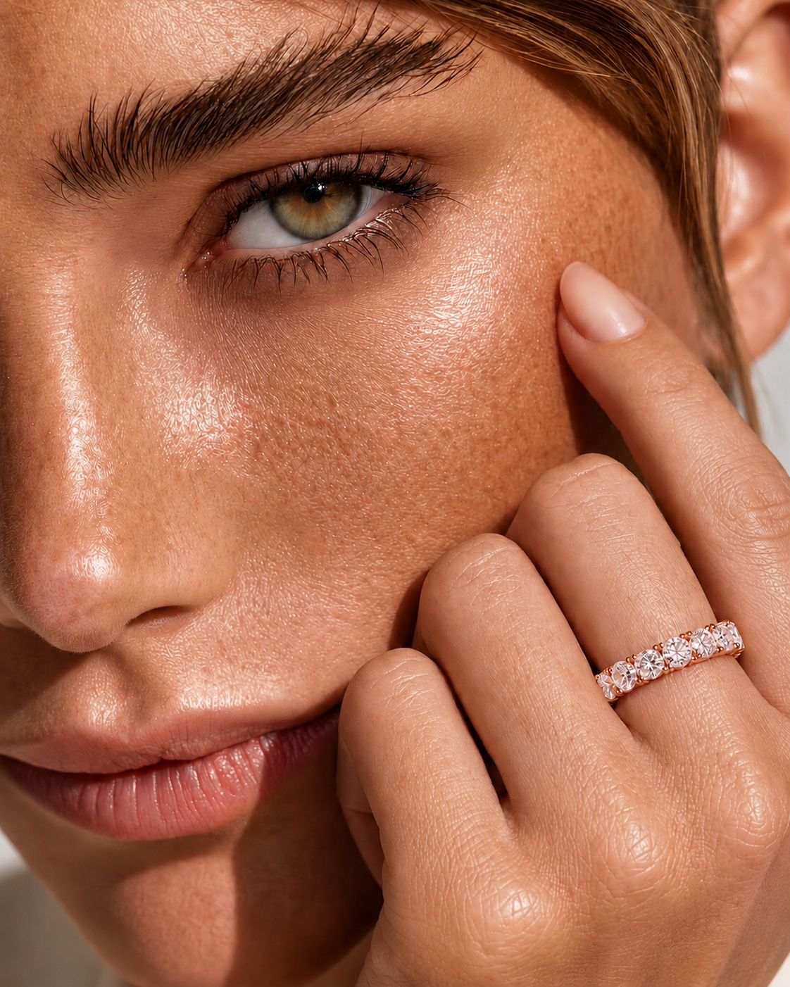 color_10K_RG, color_14K_RG &&A close-up lifestyle shot of a model wearing a diamond eternity ring on her finger, with her hand resting against her cheek.