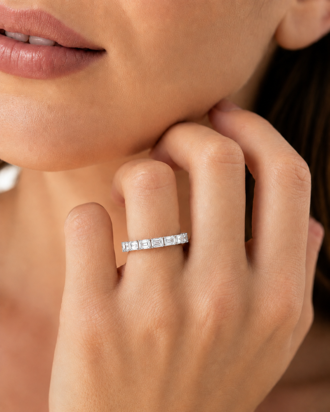 color_925_SIL,color_935_ARG,color_10K_WG, color_14K_WG &&A close-up lifestyle shot of a woman's hand resting near her chin, wearing a slim silver band ring set with baguette-cut clear gemstones.