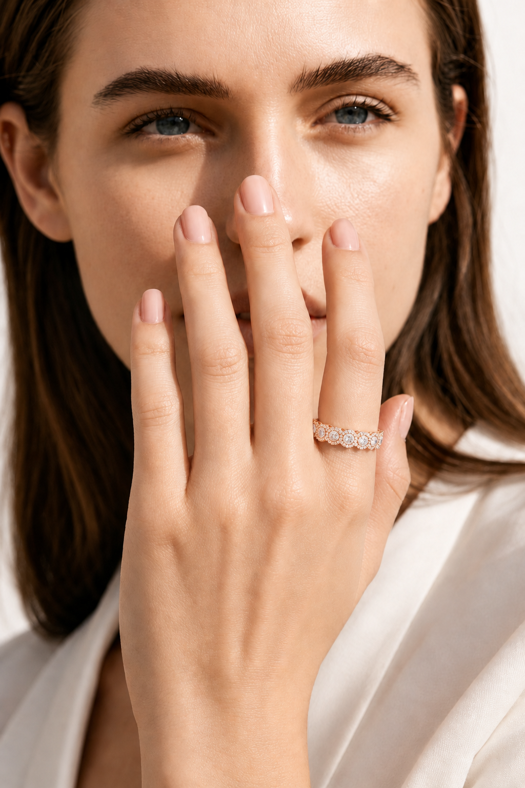 color_10K_RG, color_14K_RG &&A close-up lifestyle shot of a woman wearing a delicate diamond band ring on her finger, with her hand covering part of her face against a soft white background.