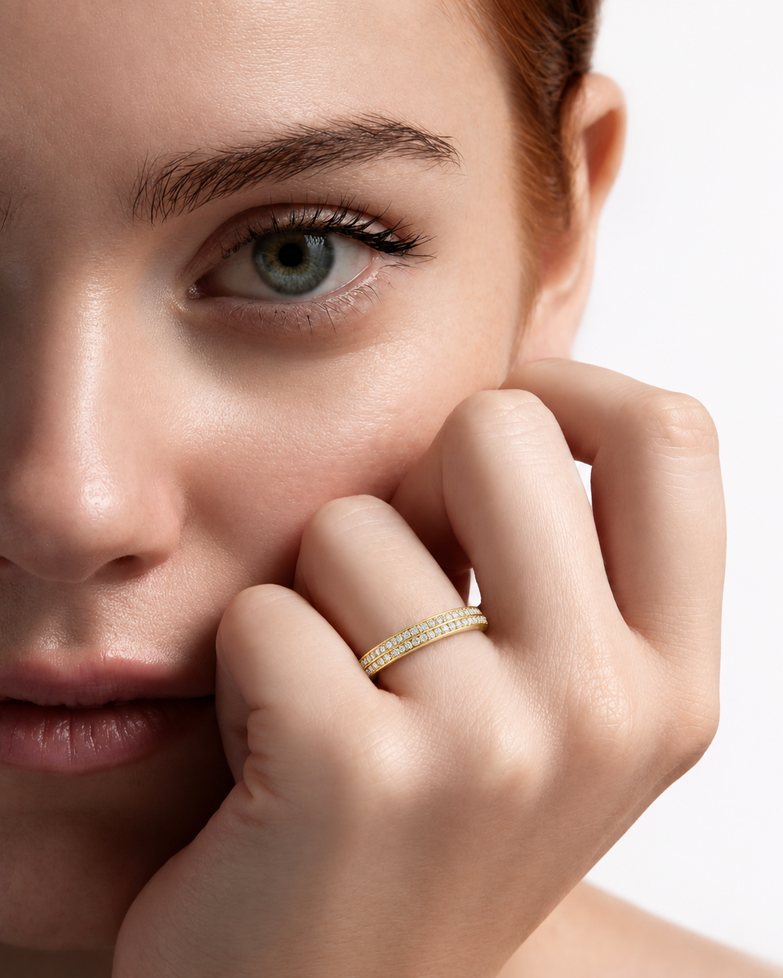 color_10K_YG, color_14K_YG &&A close-up lifestyle shot of a woman wearing a delicate yellow gold band ring set with small clear stones on her finger, with her hand resting near her face against a clean white background.