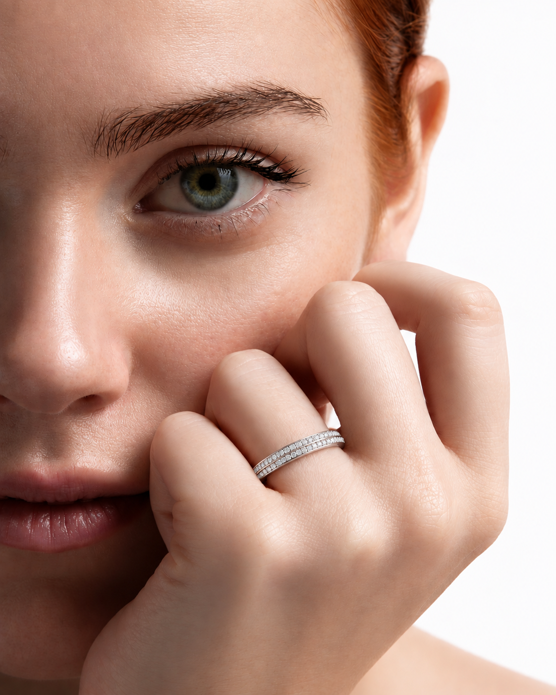 color_925_SIL,color_935_ARG,color_10K_WG, color_14K_WG &&A close-up lifestyle shot of a woman with red hair wearing a delicate silver band ring set with small clear stones, resting her hand near her face against a white background.