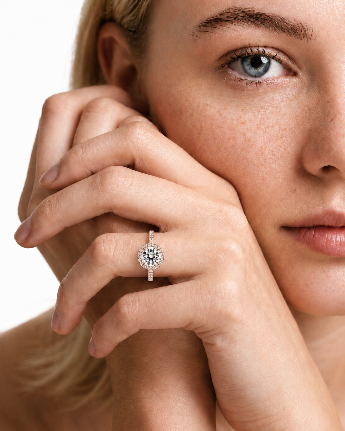 color_10K_RG, color_14K_RG &&A close-up lifestyle shot of a model wearing a diamond halo ring on her finger, with her face and hand prominently featured against a clean white background.