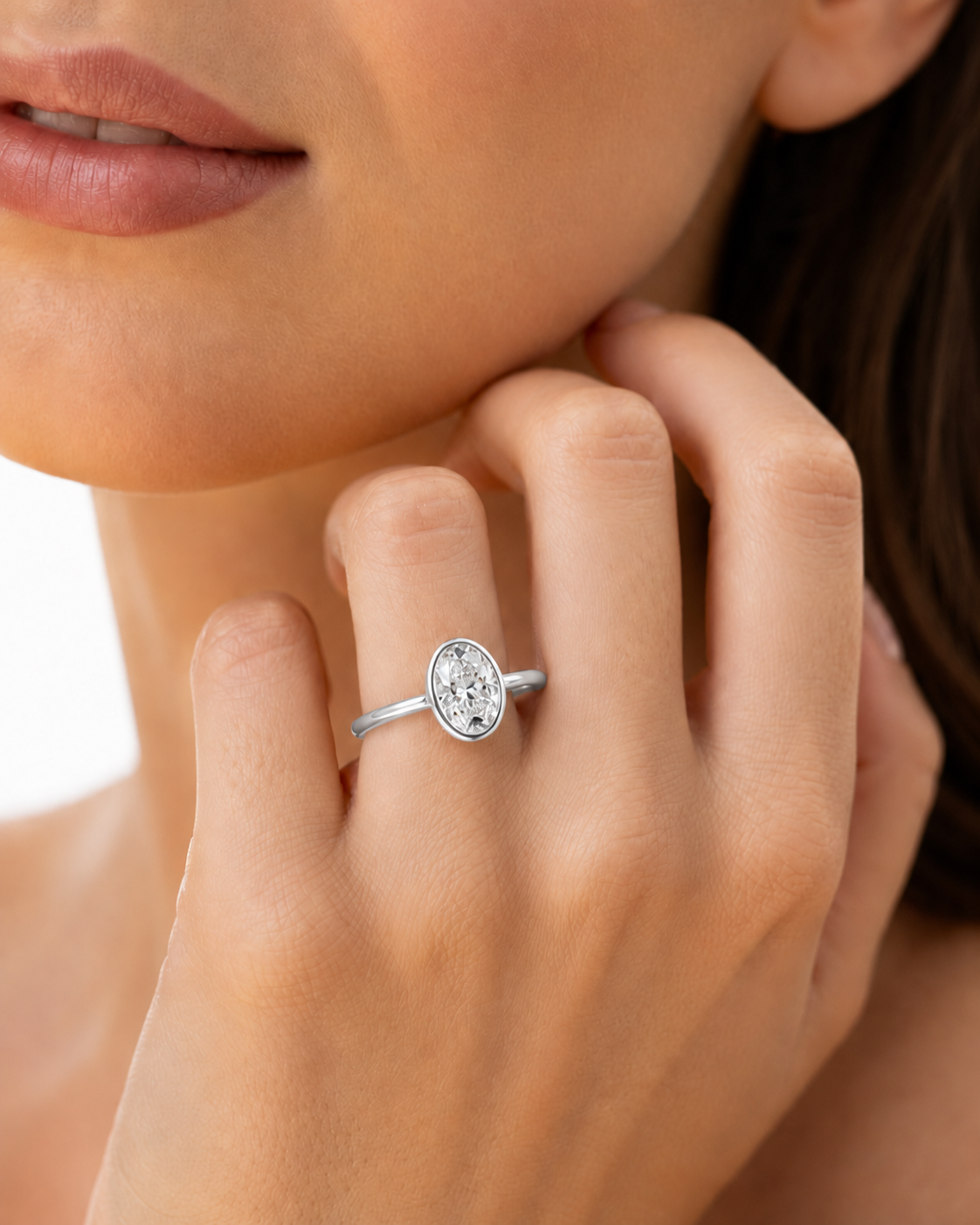 color_925_SIL,color_935_ARG,color_10K_WG, color_14K_WG &&A close-up lifestyle shot of a model wearing a silver oval ring with a clear central gemstone, set against her neck and hand.