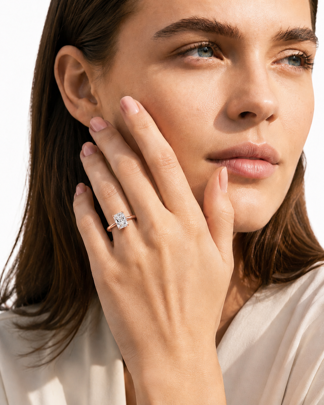 color_10K_RG, color_14K_RG &&A close-up lifestyle shot of a woman with her hand resting on her cheek, wearing a rose gold ring with a square-cut diamond.