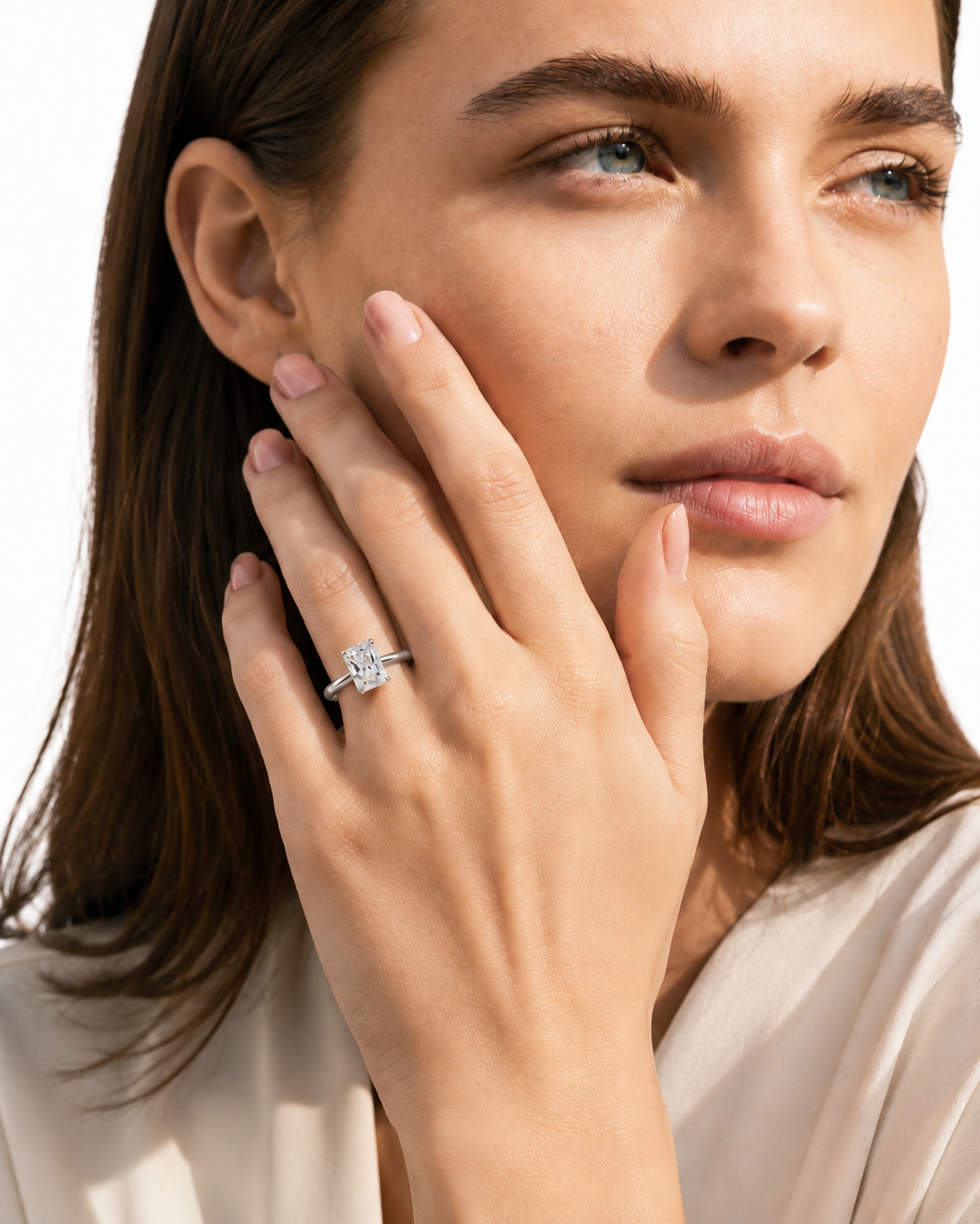 color_925_SIL,color_935_ARG,color_10K_WG, color_14K_WG &&A close-up lifestyle shot of a woman with her hand resting on her cheek, wearing a yellow gold engagement ring with a round brilliant-cut diamond. The background is a clean white studio backdrop.