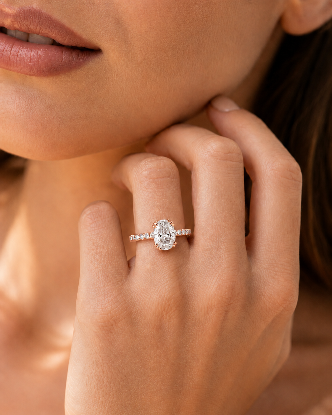 color_10K_RG, color_14K_RG &&A close-up lifestyle shot of a woman wearing a diamond engagement ring on her finger. The ring features a pear-cut center stone surrounded by a halo, with a pavé band set with small round diamonds.