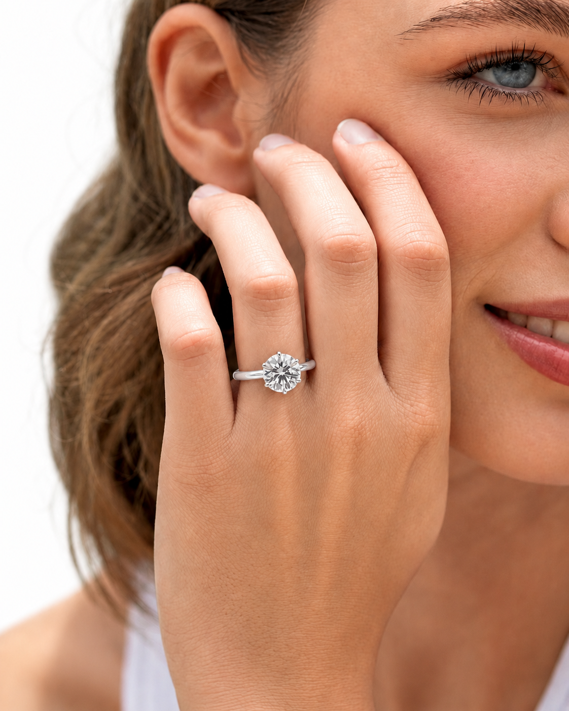 color_925_SIL,color_935_ARG,color_10K_WG, color_14K_WG &&A close-up lifestyle shot of a woman wearing a silver-toned diamond engagement ring on her finger, with her hand resting against her cheek against a clean white background.