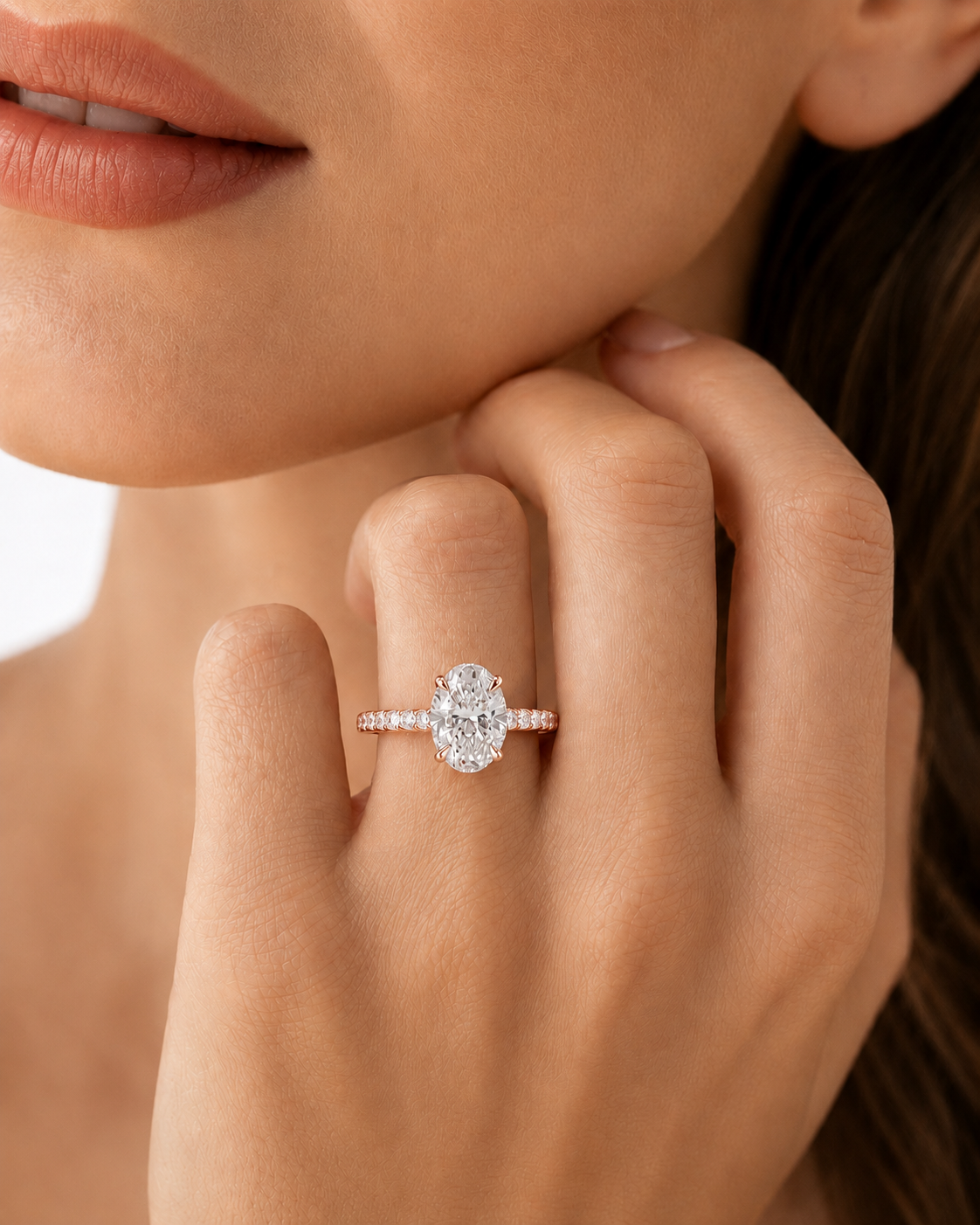 color_10K_RG, color_14K_RG &&A close-up lifestyle shot of a model's hand wearing a silver-toned engagement ring with a round brilliant-cut center stone and a pavé band, set against her skin and lips.