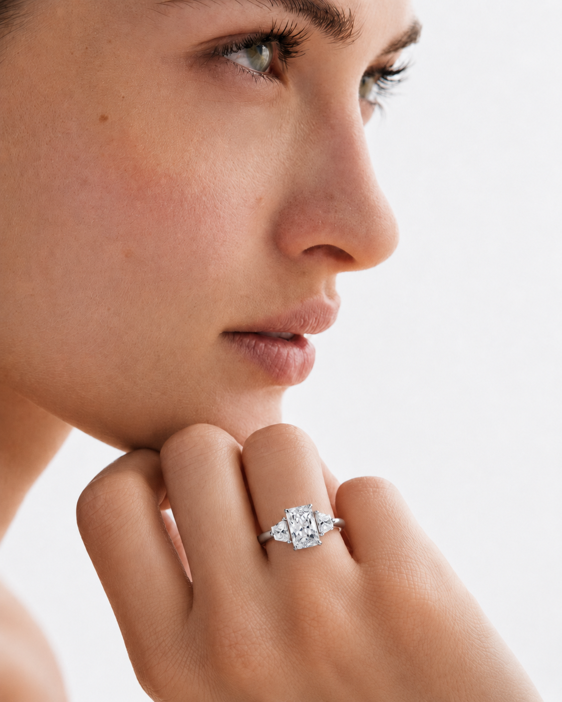 color_925_SIL,color_935_ARG,color_10K_WG, color_14K_WG &&A close-up lifestyle shot of a model wearing a silver-toned diamond ring with a square-cut center stone and smaller surrounding stones on her finger.