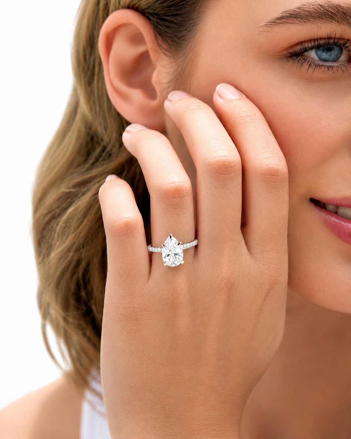 color_925_SIL,color_935_ARG,color_10K_WG, color_14K_WG &&A close-up lifestyle shot of a woman wearing a silver ring with a pear-cut clear gemstone on her finger, with her hand resting near her face against a white background.